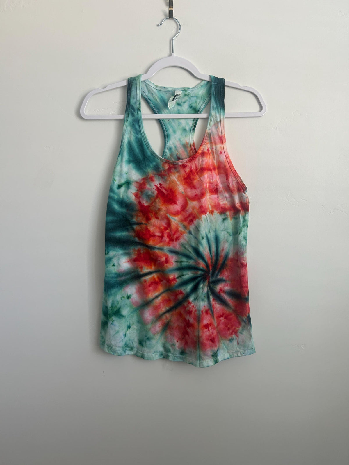 Full front view of a one of a kind teal and red spiral ice dye racerback tank on a hanger.