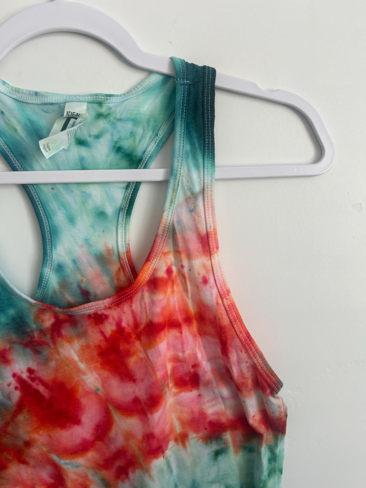 Detail of the racerback neckline on a hand dyed tank, teal green fading into a red and orange ice dye spiral.