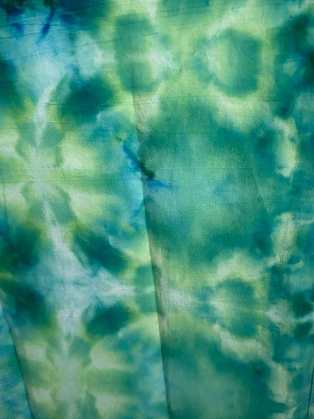 Close-up of a green, teal, and blue ice dye tea towel showing a soft cloudy watercolor tie dye pattern.