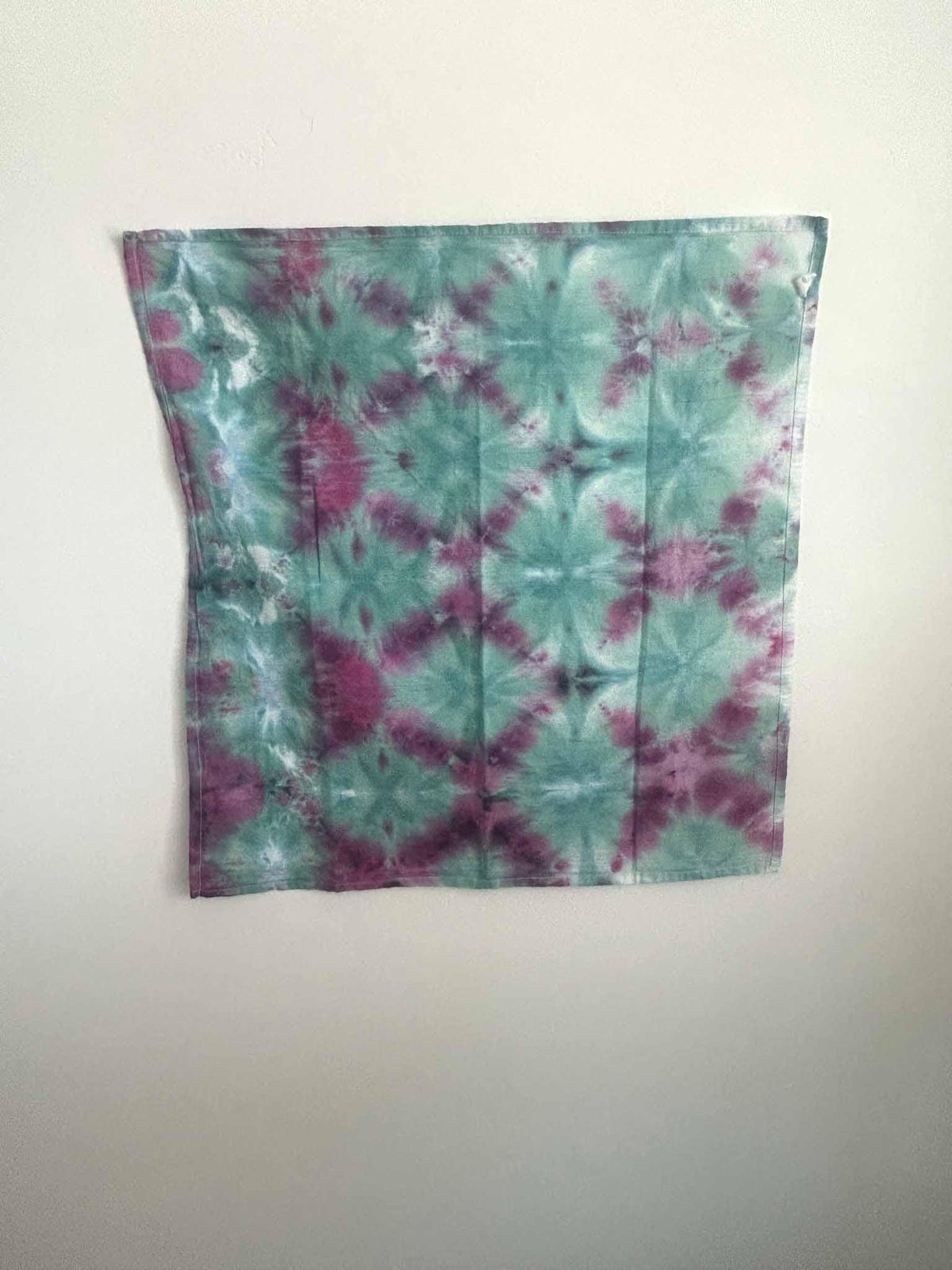 Full view of a one of a kind ice dye tea towel in soft teal green with raspberry and magenta blooms.