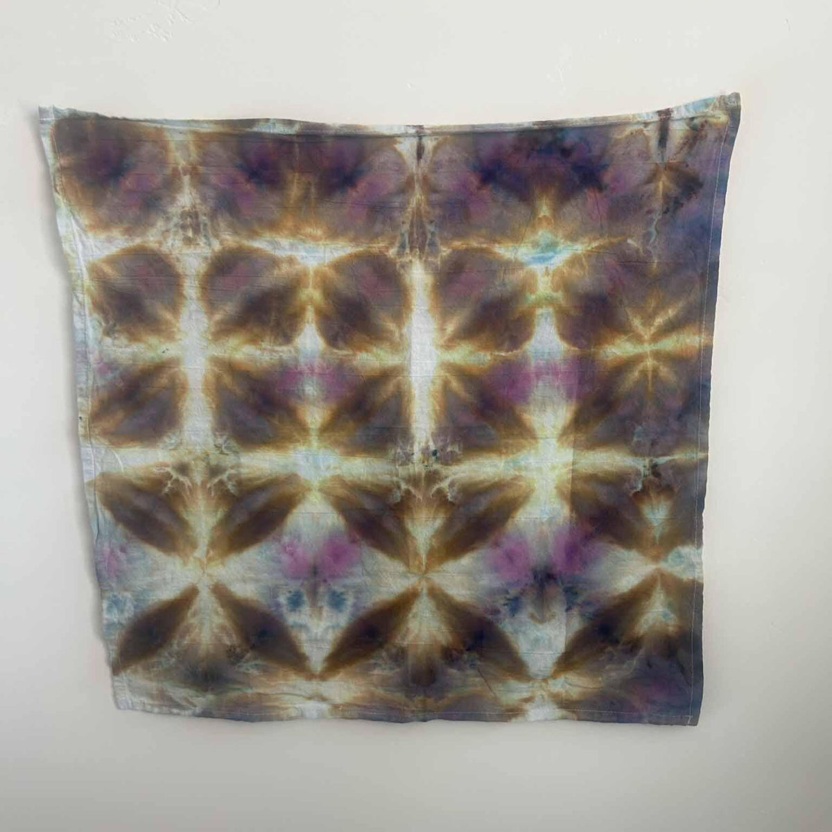 Black opal ice dye tea towel in purple, gold, and blue star pattern, full view hanging