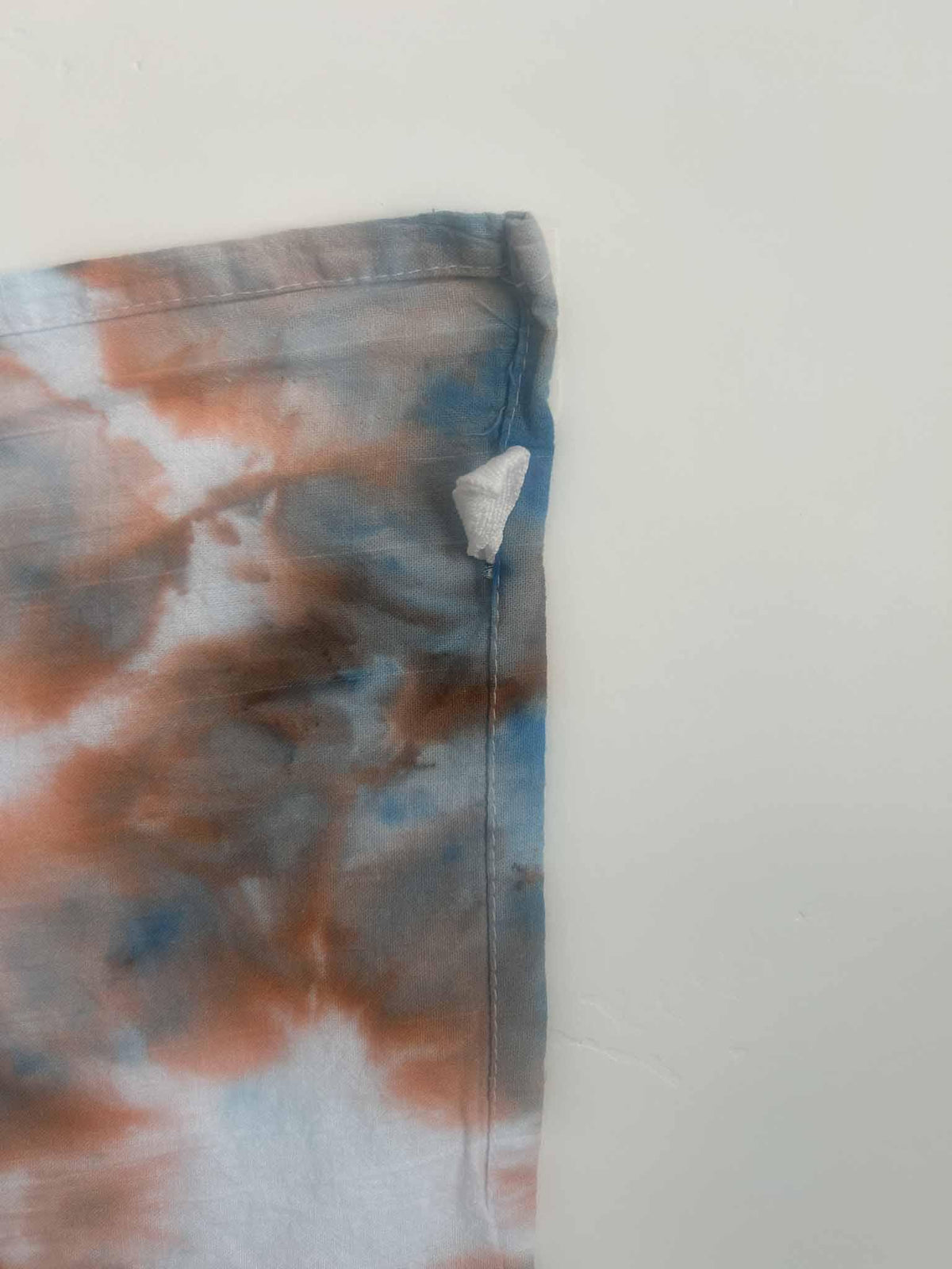 Close-up of ice dye tea towel corner showing hang loop and rust blue color blending