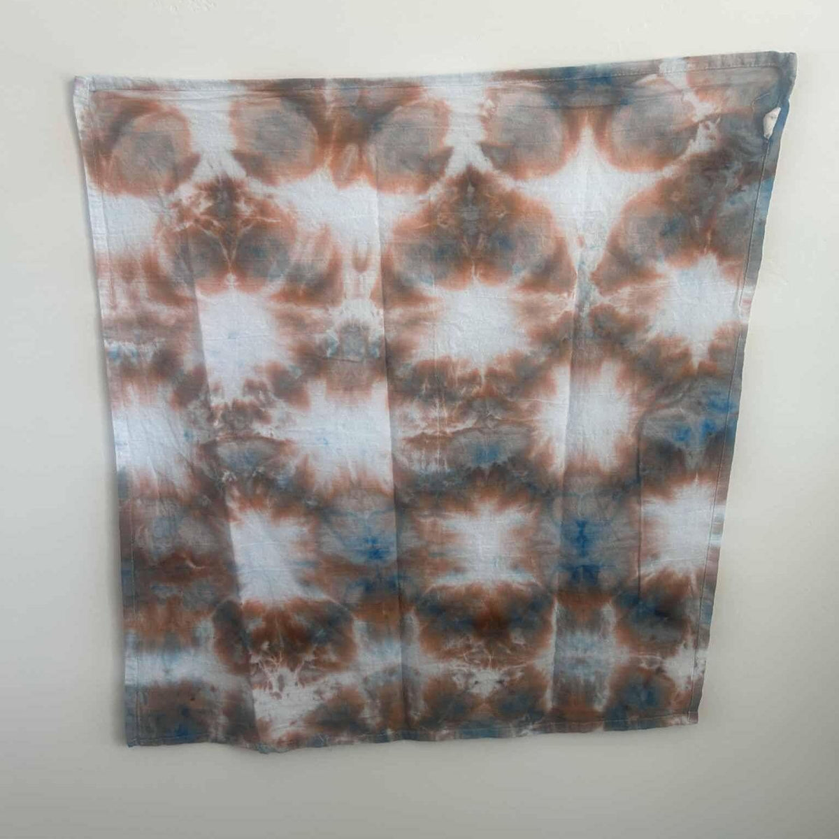 Rust and blue ice dye tea towel with sunburst pattern, full view hanging on wall