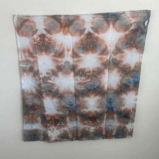Rust and blue ice dye tea towel with sunburst pattern, full view hanging on wall
