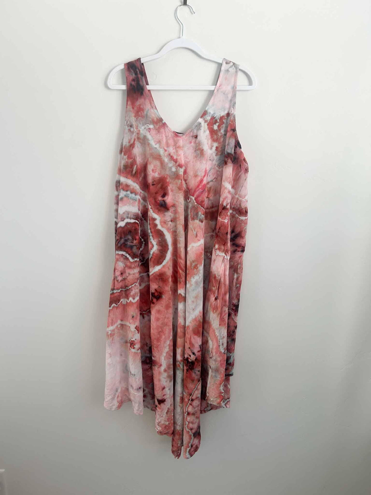 Full view of deep red and blush ice dyed hi-lo tank dress hanging against a white wall