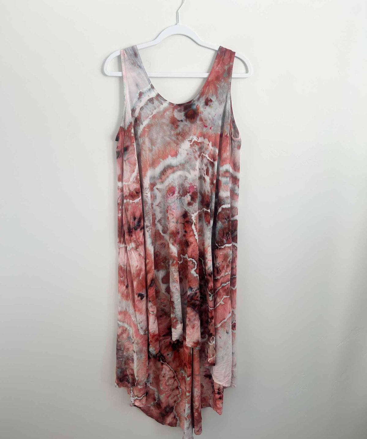 Ice dyed rayon hi-lo dress in deep red and rust geode pattern hanging on a white hanger against a white wall