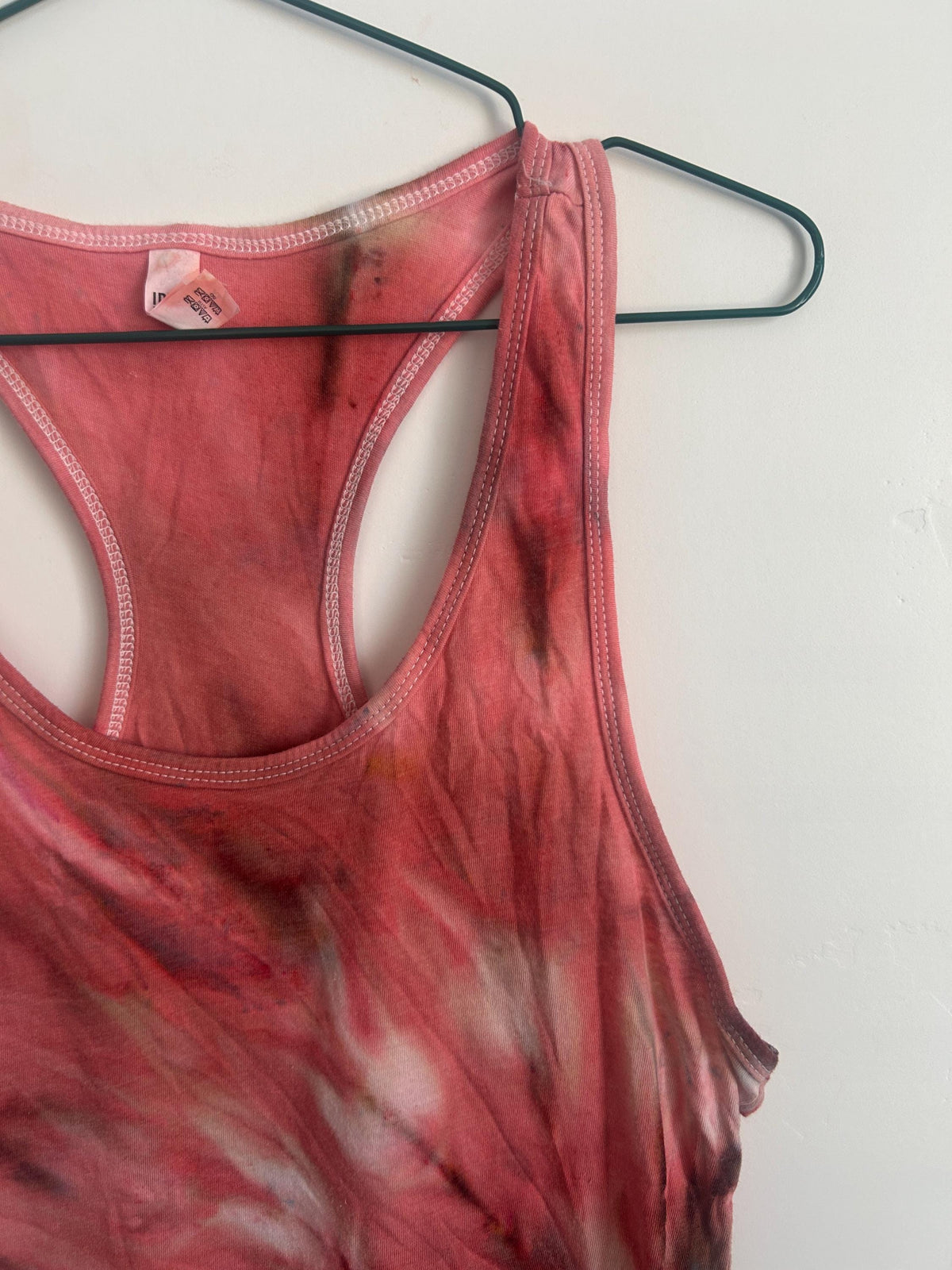 Back view of a Bloodmoon ice dye racerback tank top on a hanger, showing the racerback cut and marbled coral, rose, and charcoal tie dye pattern.