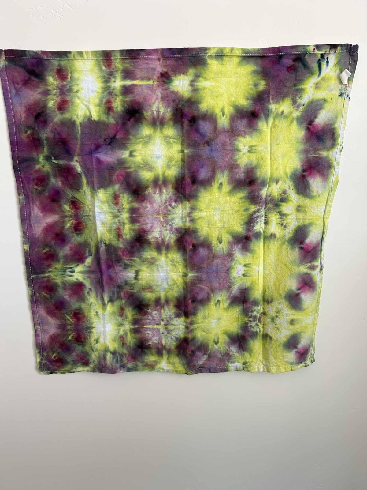 Full view of a one of a kind ice dye tea towel in bright chartreuse yellow with deep purple, plum, and magenta.