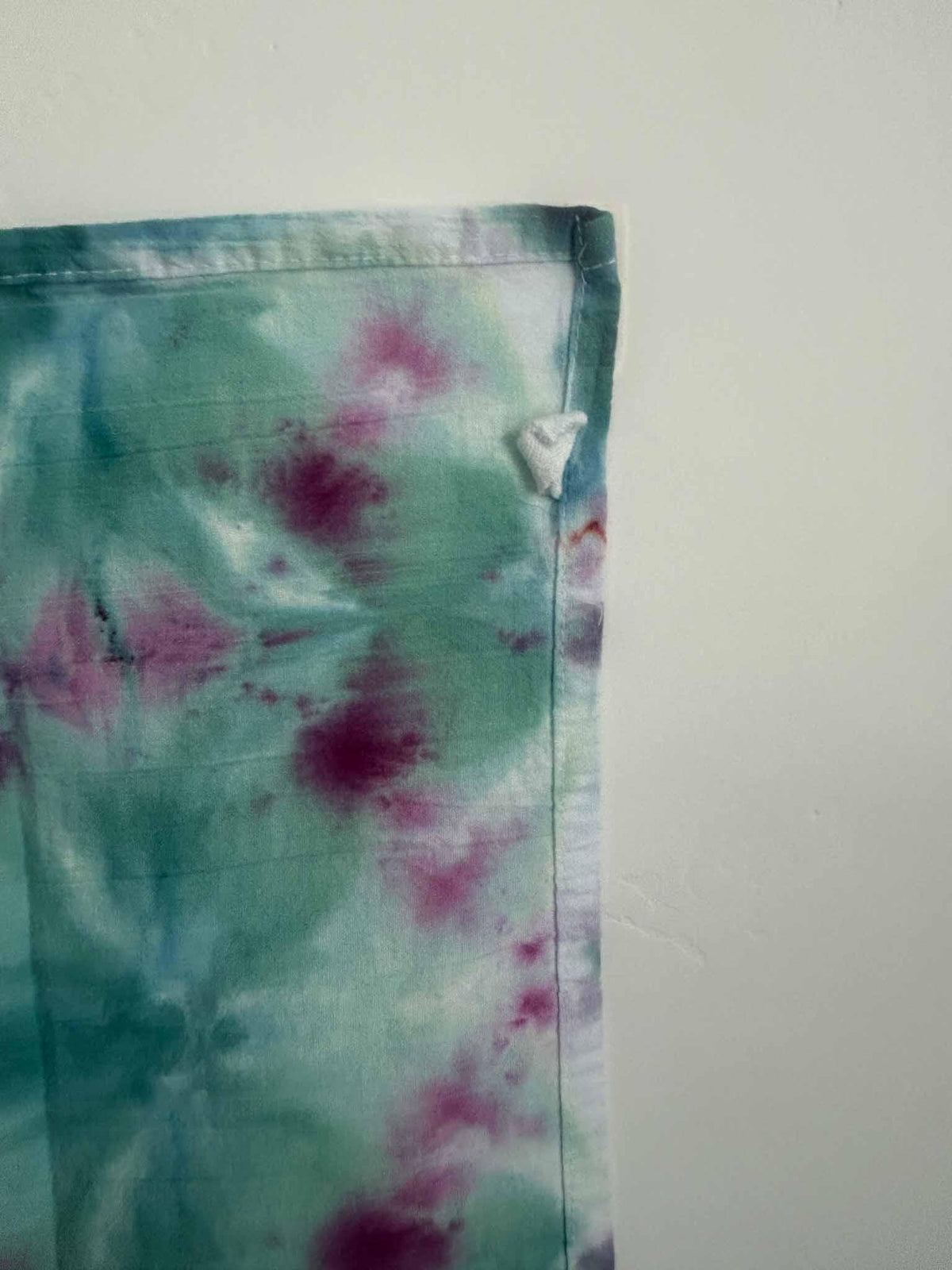 Detail of a hand dyed teal and magenta tea towel showing the hemmed edge and white corner hang loop.