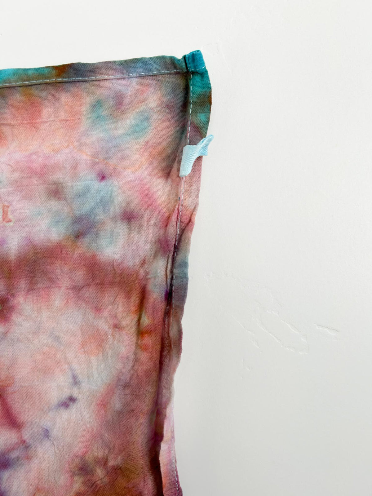 Corner detail of rose turquoise ice dyed tea towel showing hang loop
