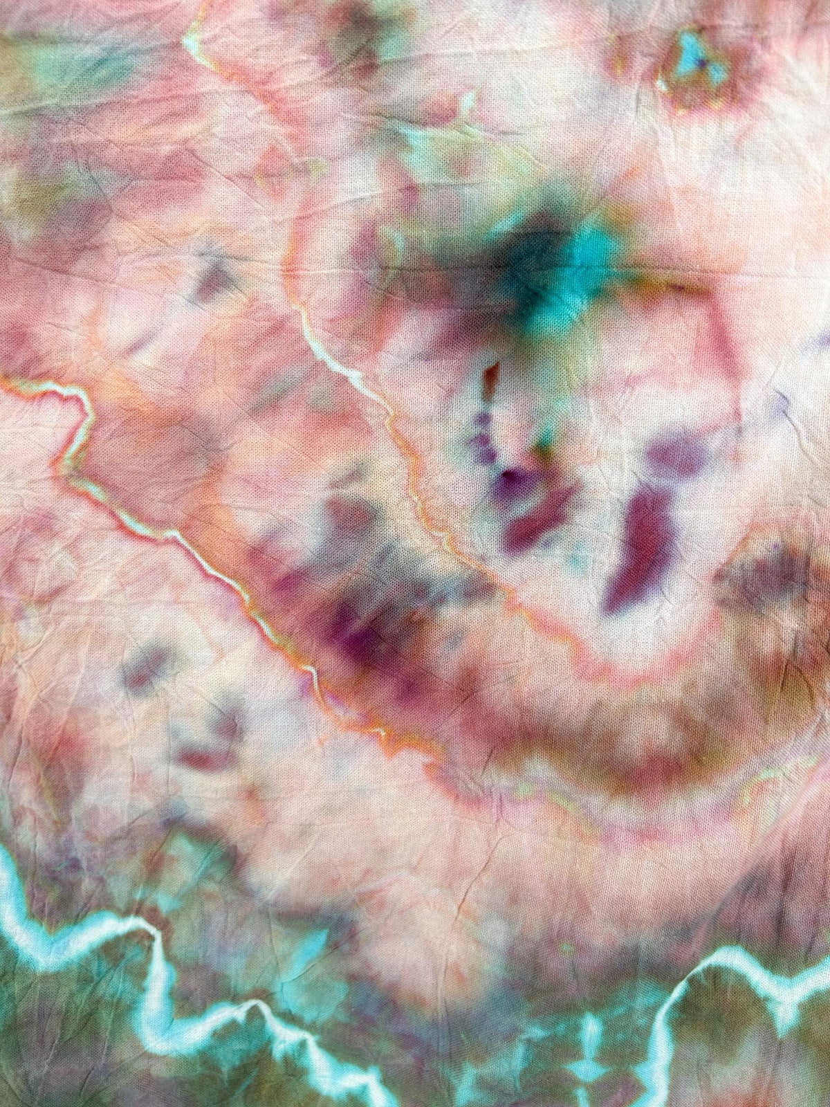 Close-up of ice dyed tea towel showing rose, burgundy, and turquoise marbled veining