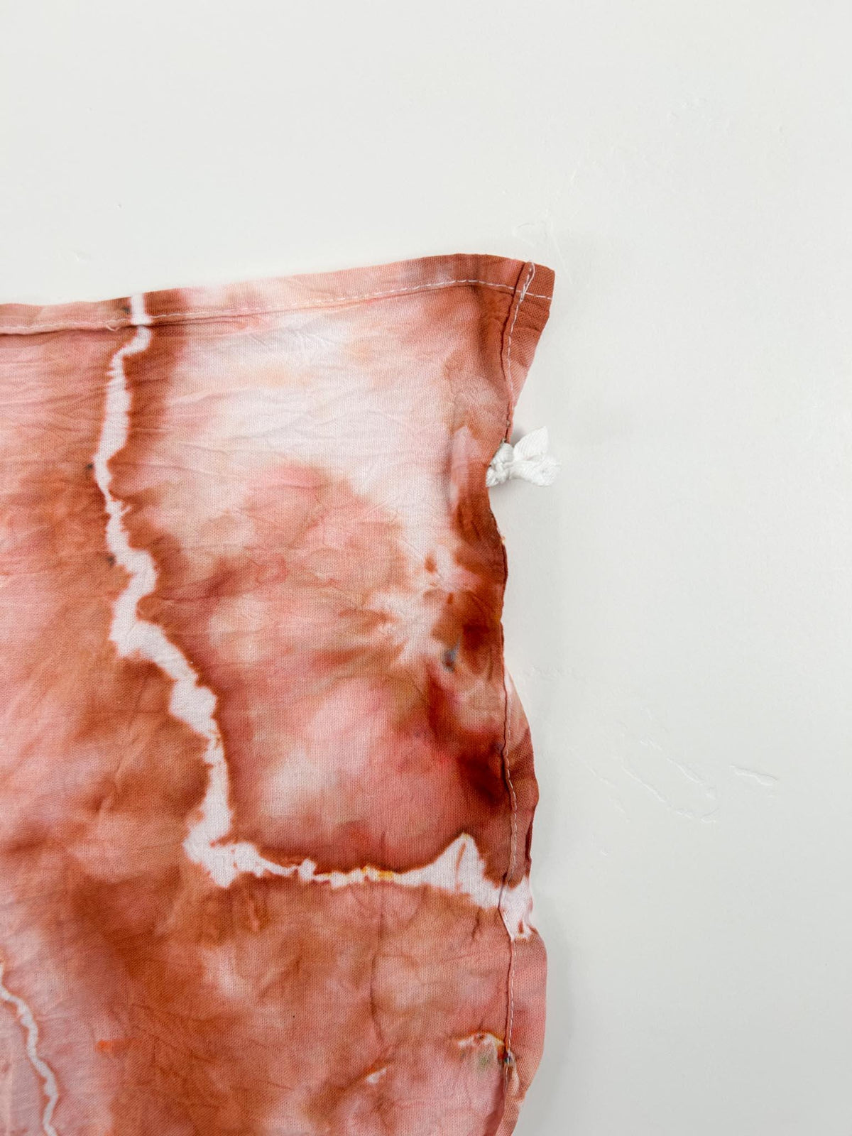 Corner detail of rust terracotta ice dyed tea towel showing hang loop