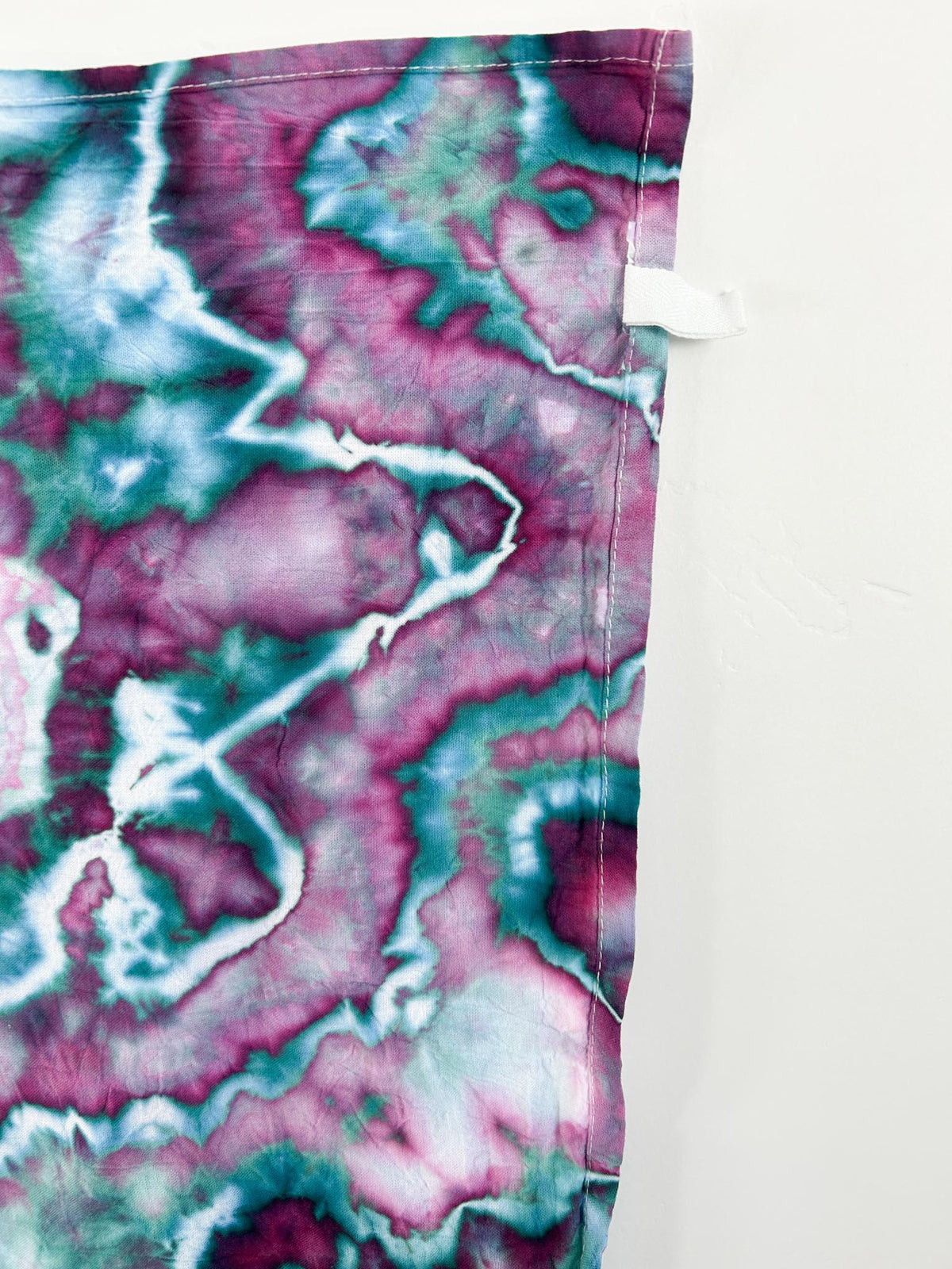 Corner detail of magenta emerald ice dyed tea towel showing hang loop