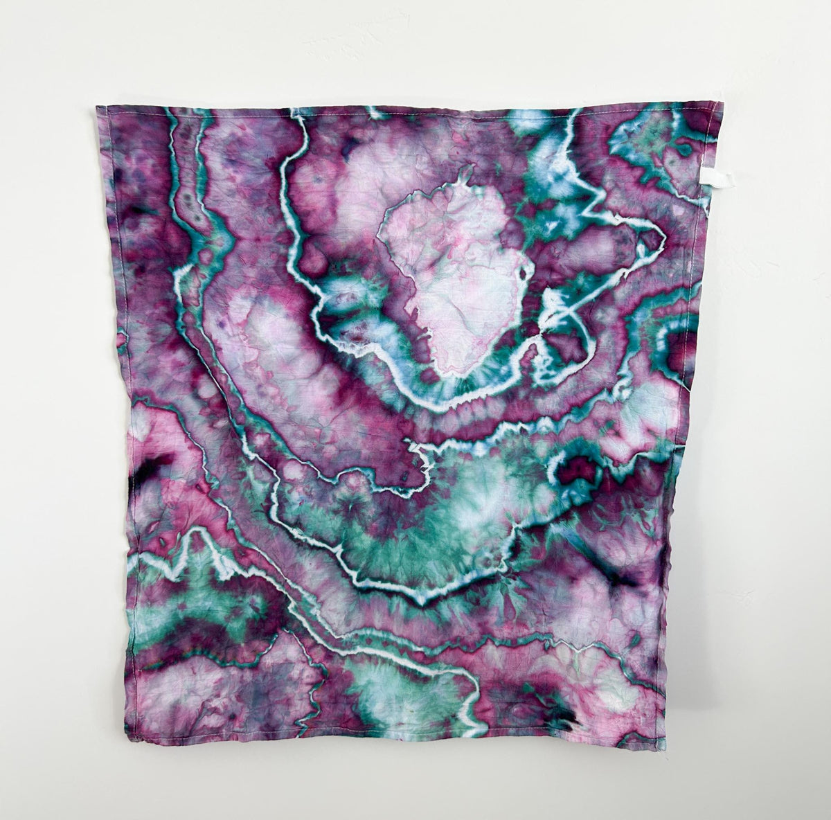 Ice dyed cotton tea towel hanging flat, full view of magenta emerald marbled pattern