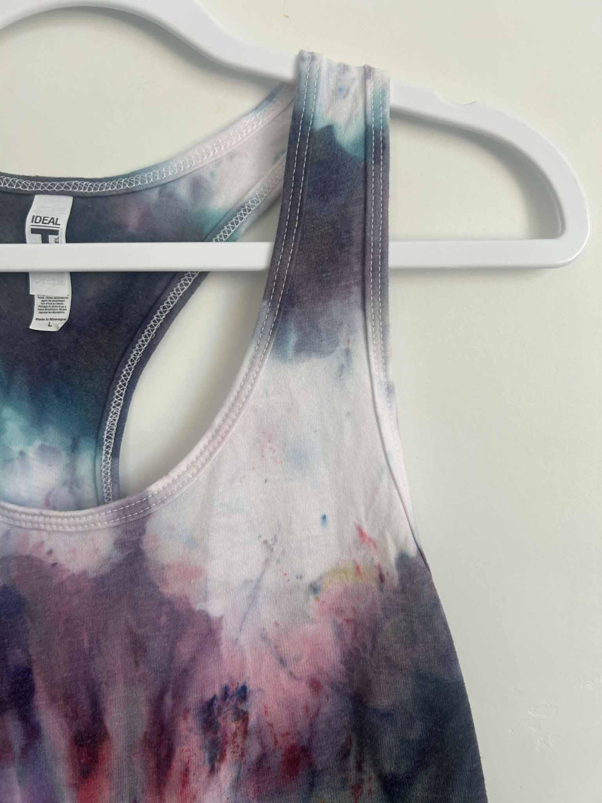 Tie dye tank top racerback strap detail with Next Level Ideal T tag in purple and teal