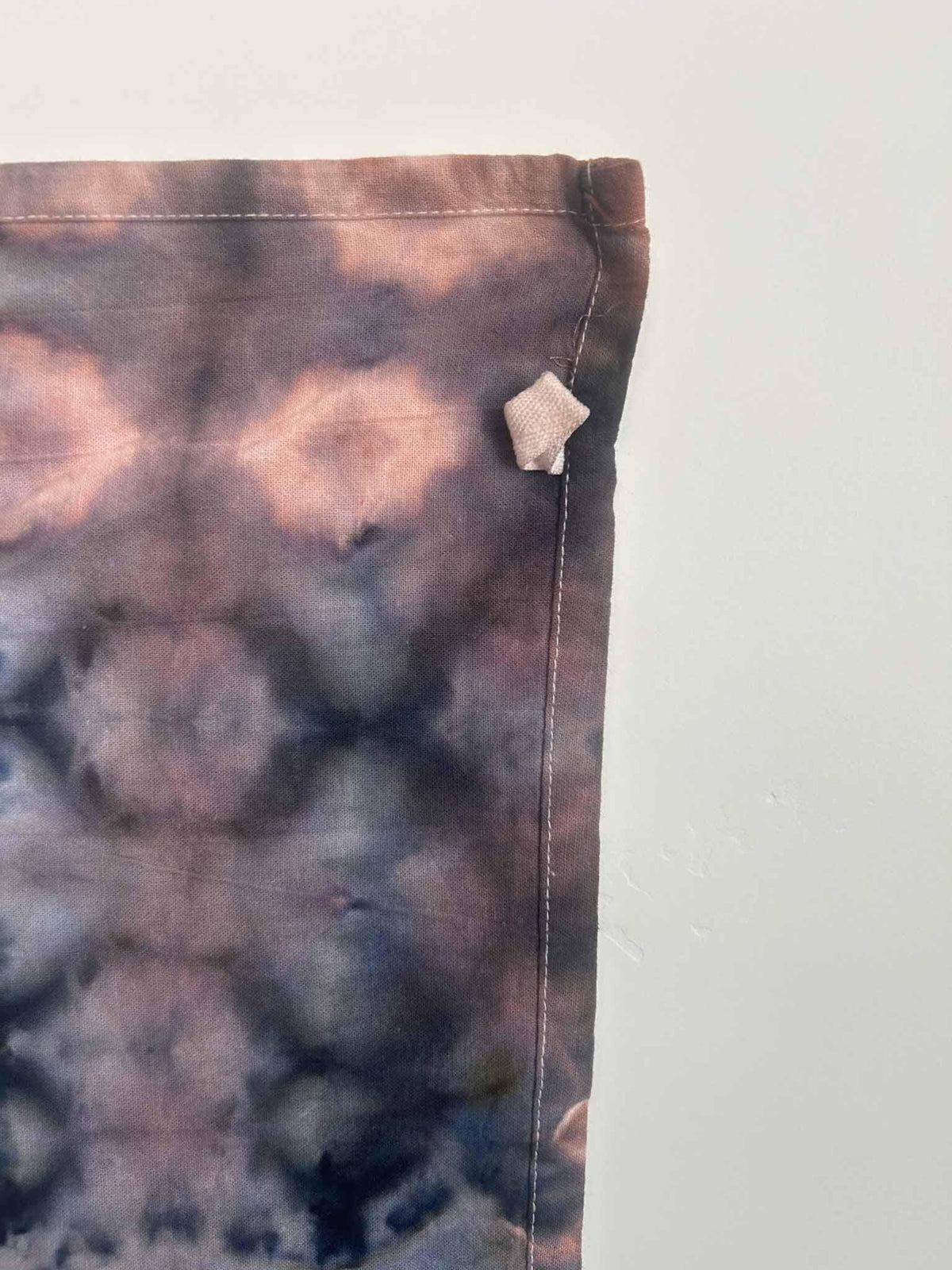 Close-up of ice dye tea towel corner and hem showing rust and indigo color blending