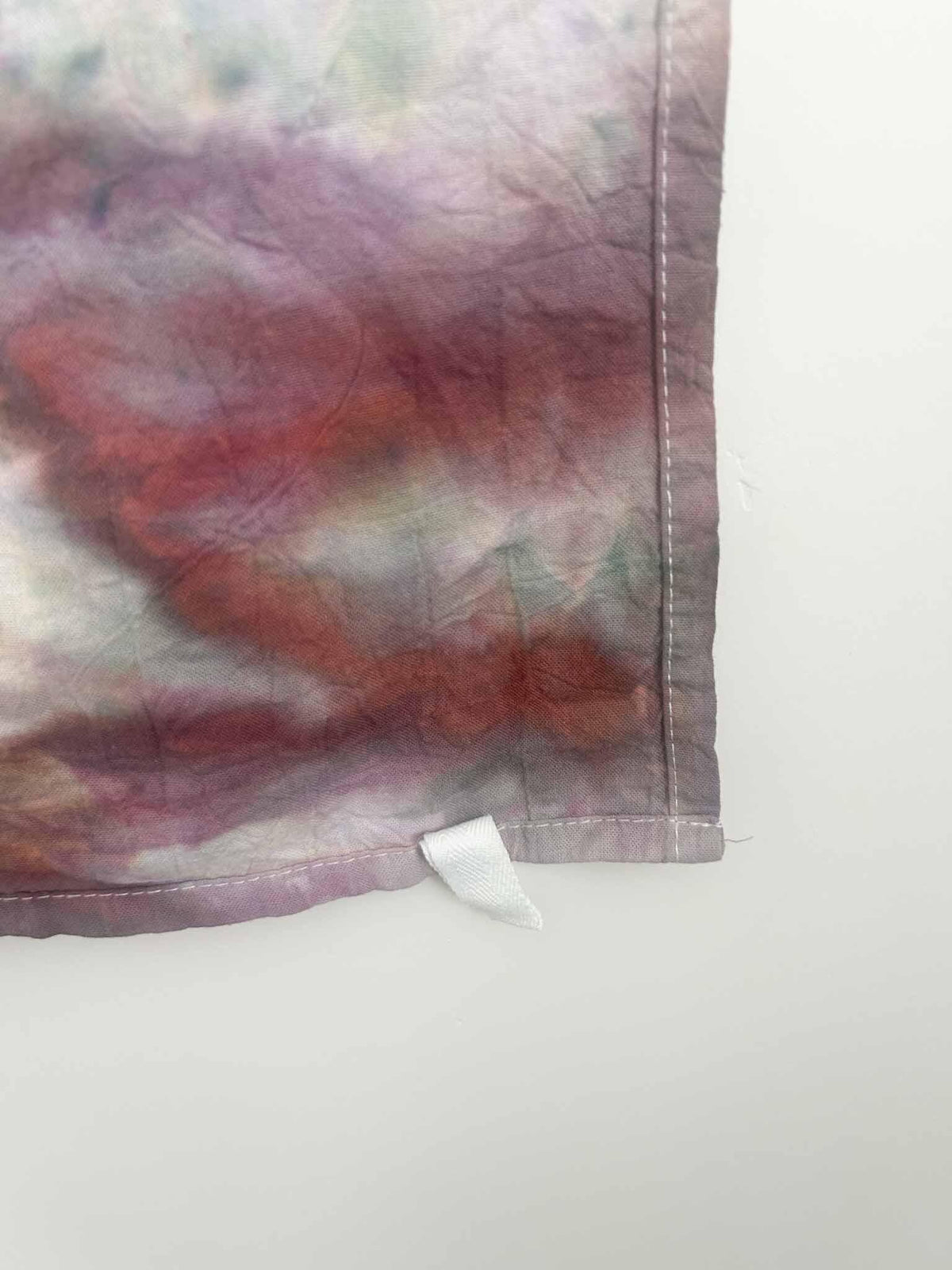 Corner detail of ice dyed tea towel showing hem stitching and white hang loop