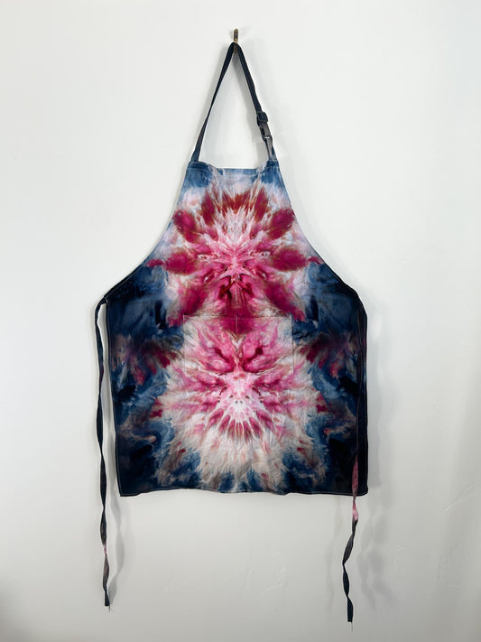 Navy burgundy tie dye apron hanging on hook, full view with adjustable strap and pocket