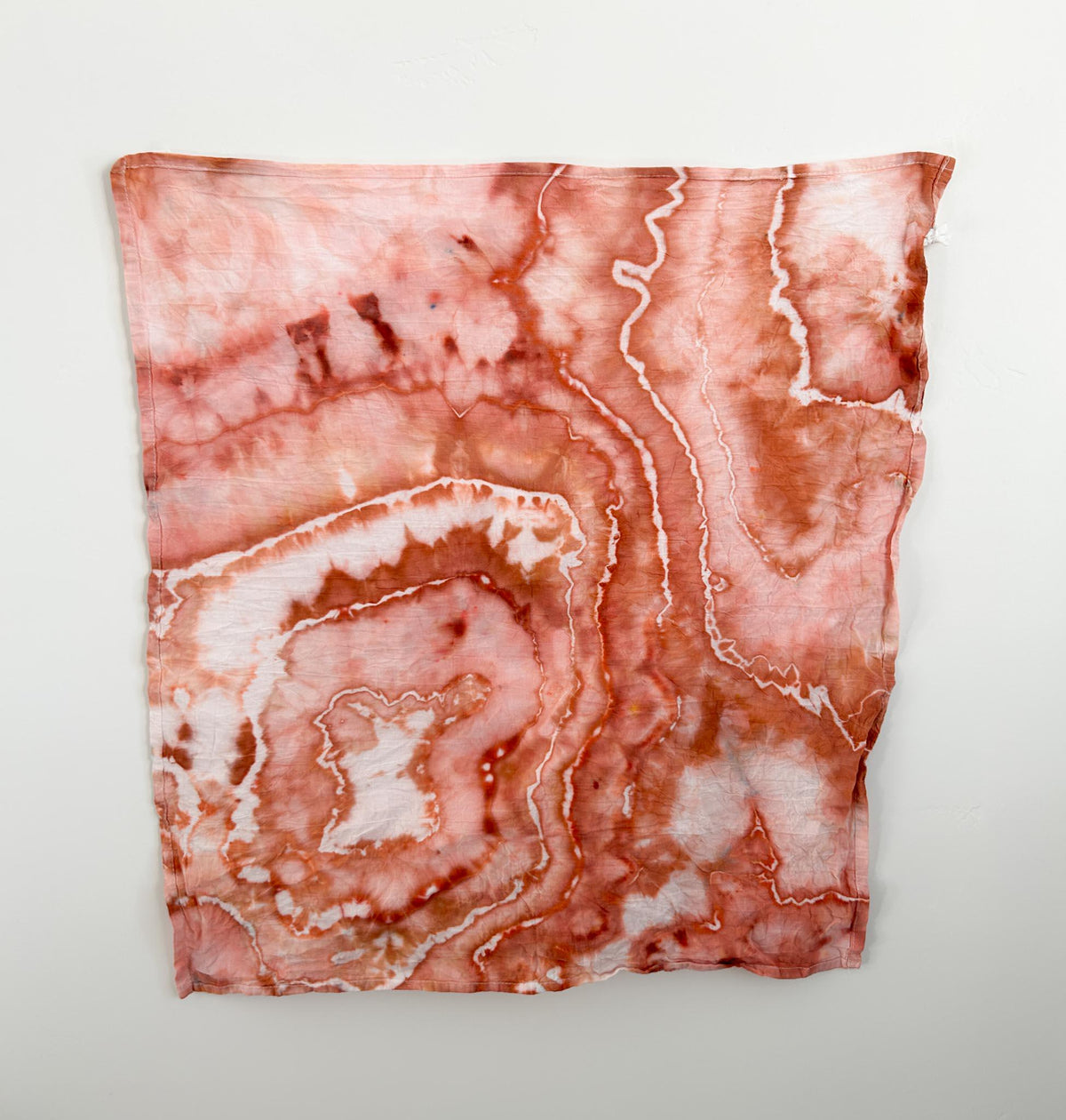 Ice dyed cotton tea towel hanging flat, full view of rust terracotta marbled pattern