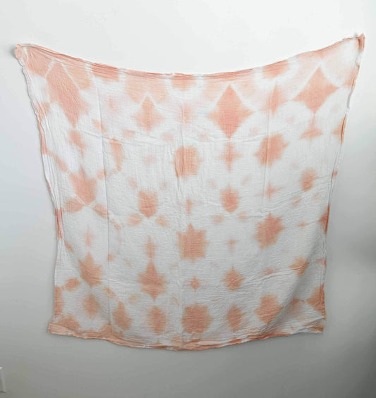 Peach and white shibori diamond pattern swaddle blanket hanging flat against a white wall