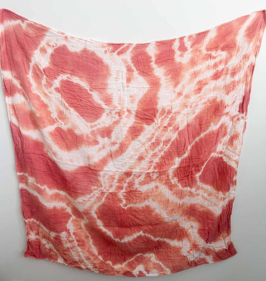 Coral red and white swirled tie dye swaddle blanket hanging flat against a white wall