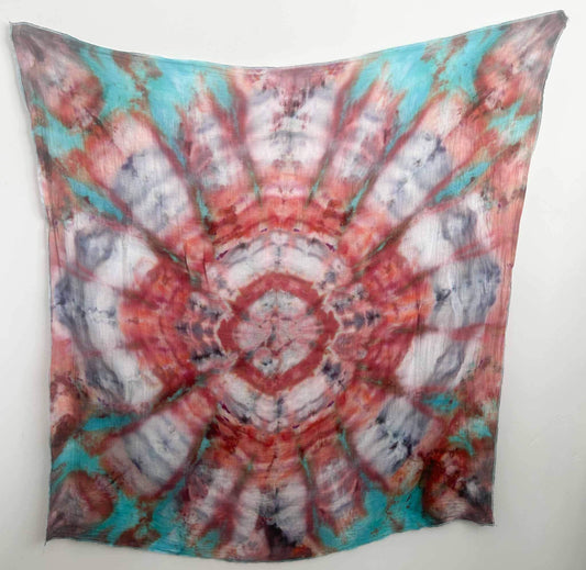 Coral, teal, and red kaleidoscope mandala tie dye swaddle blanket hanging flat against a white wall