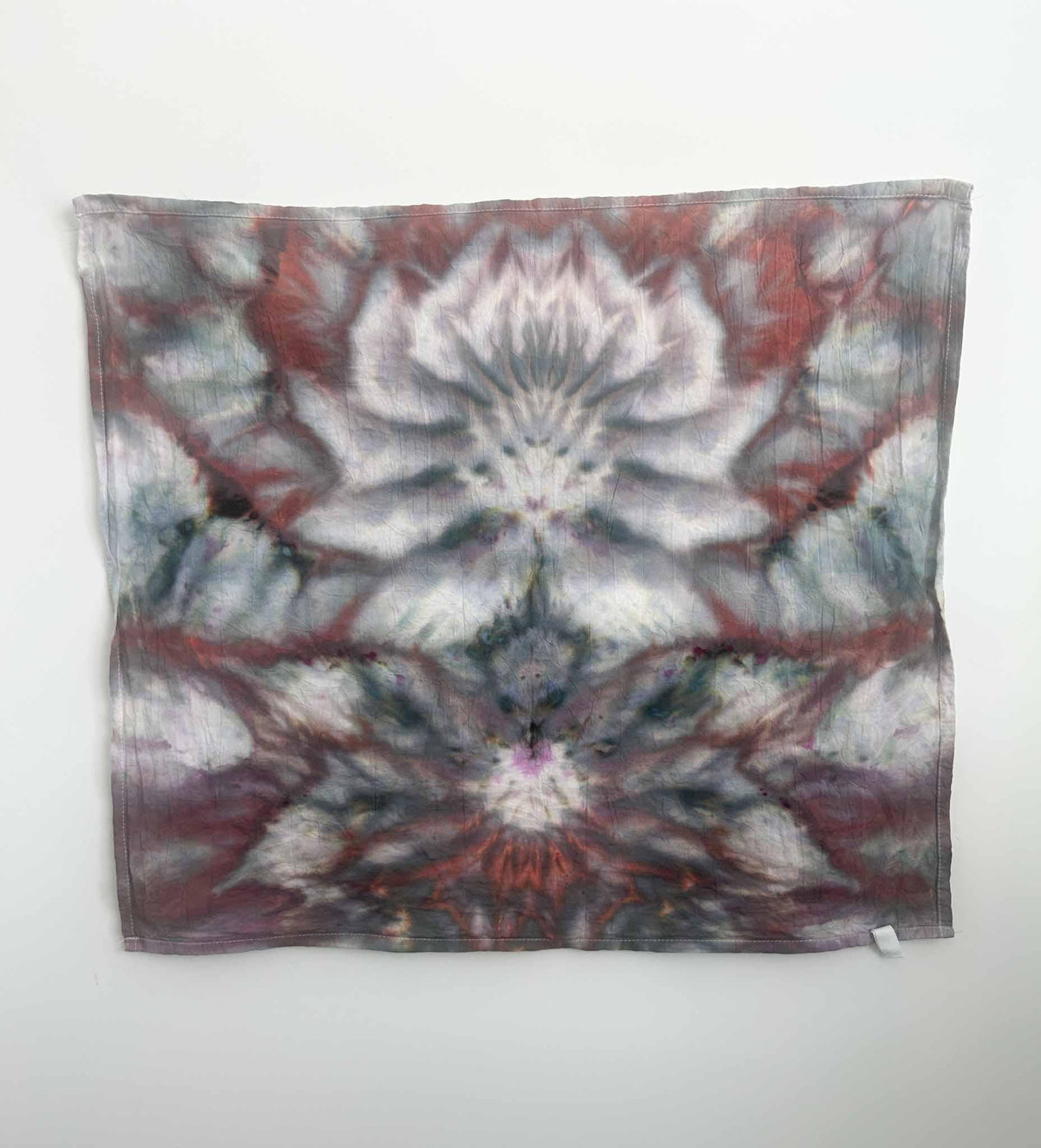 Dusty rose sage and rust ice dyed cotton tea towel hanging flat against white wall