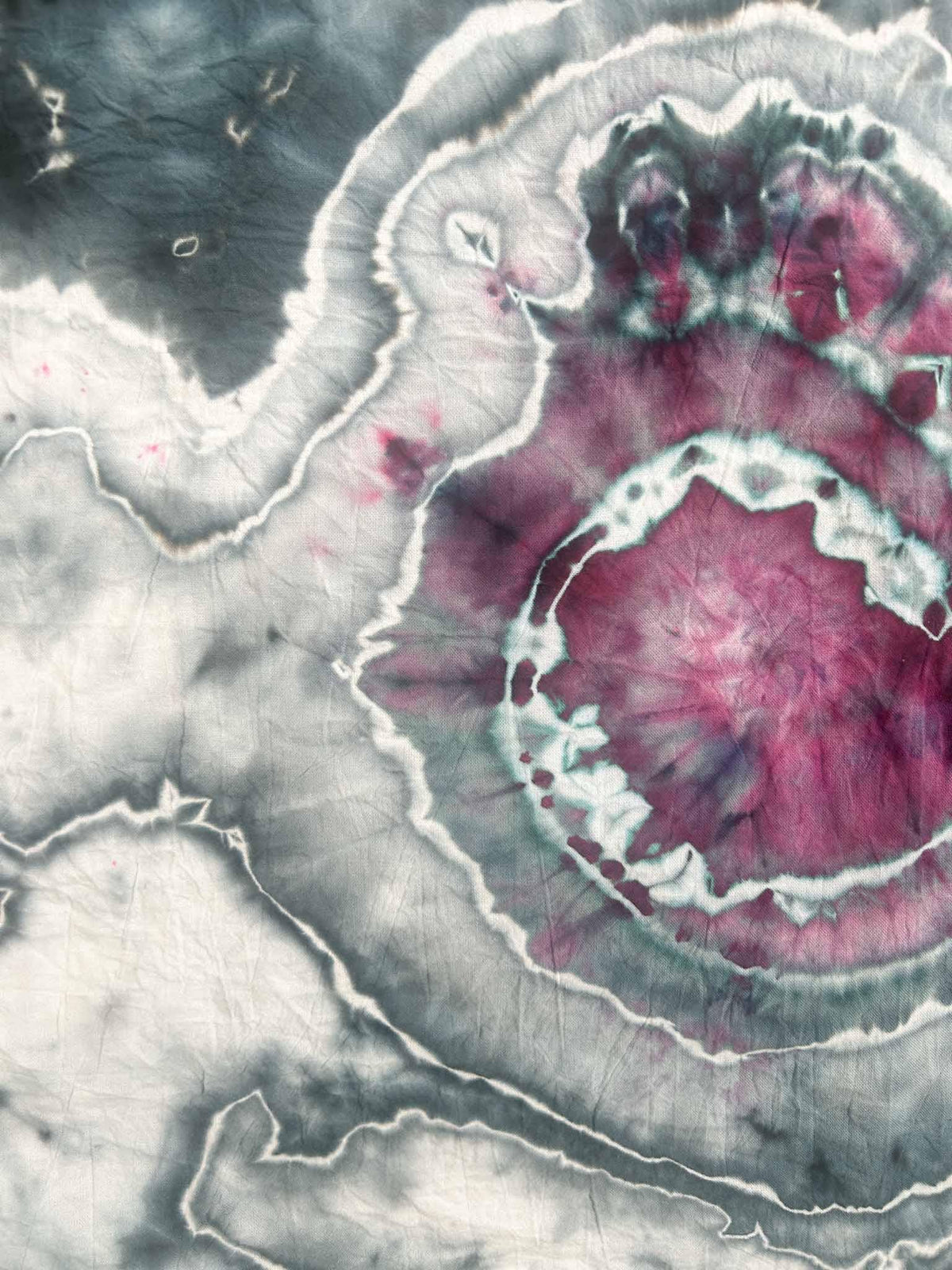 Close up of magenta spiral center on slate blue ice dyed tea towel showing crackled white veining