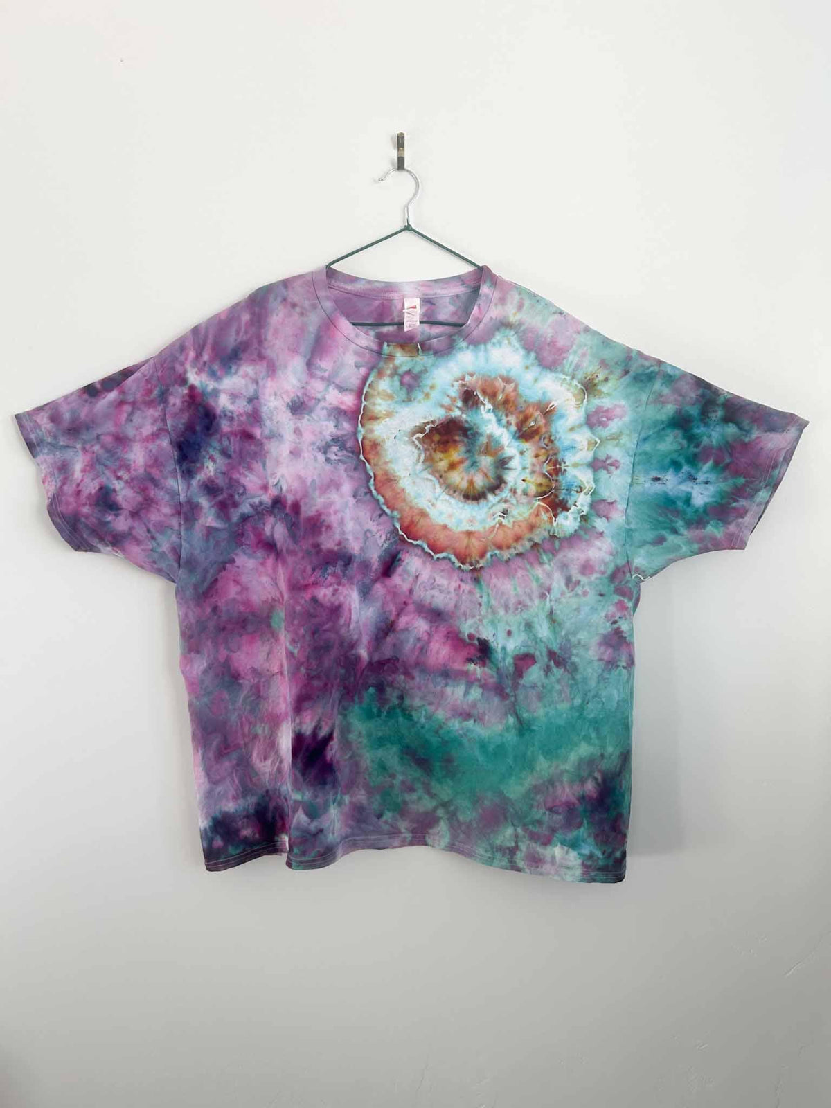 Purple teal and rust geode tie dye t-shirt hanging on hanger against white wall