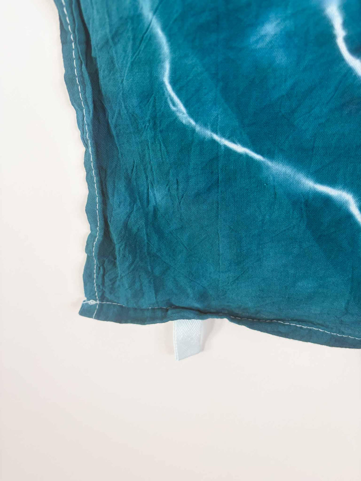 Corner detail of teal tie dye tea towel showing hang loop and stitched hem
