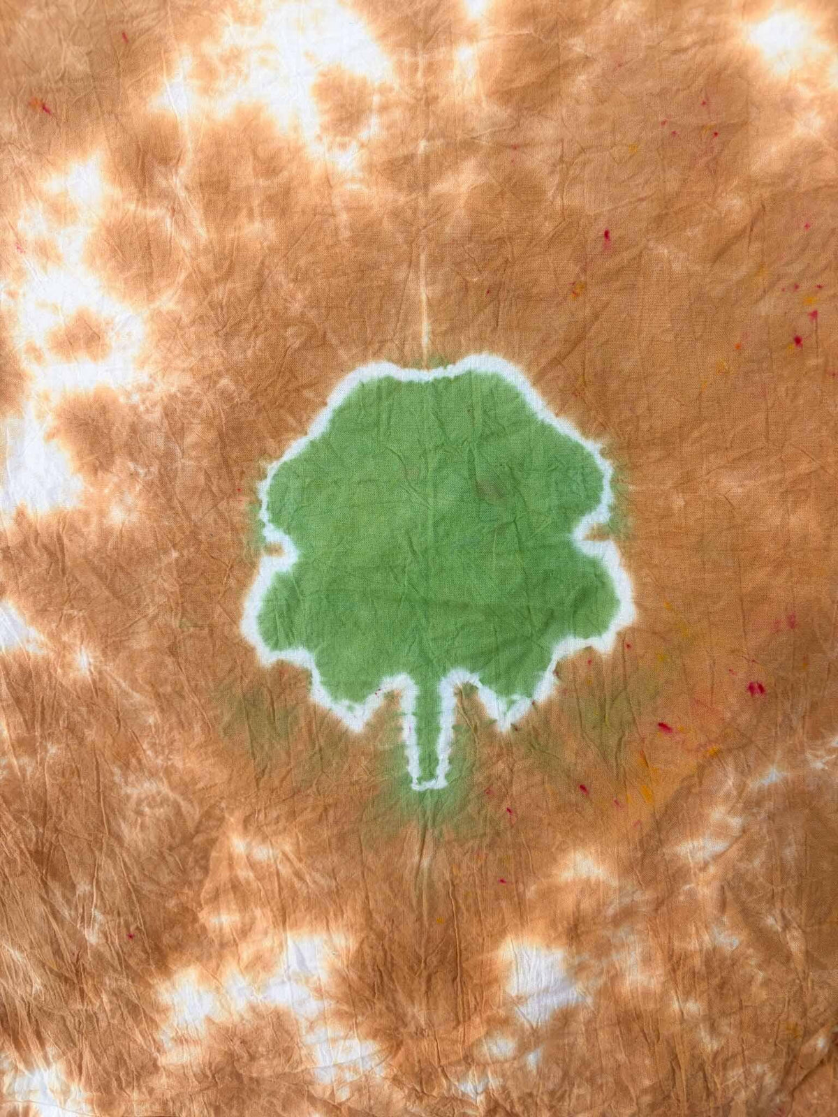 Close-up of green four leaf clover tie dye on rust brown cotton tea towel