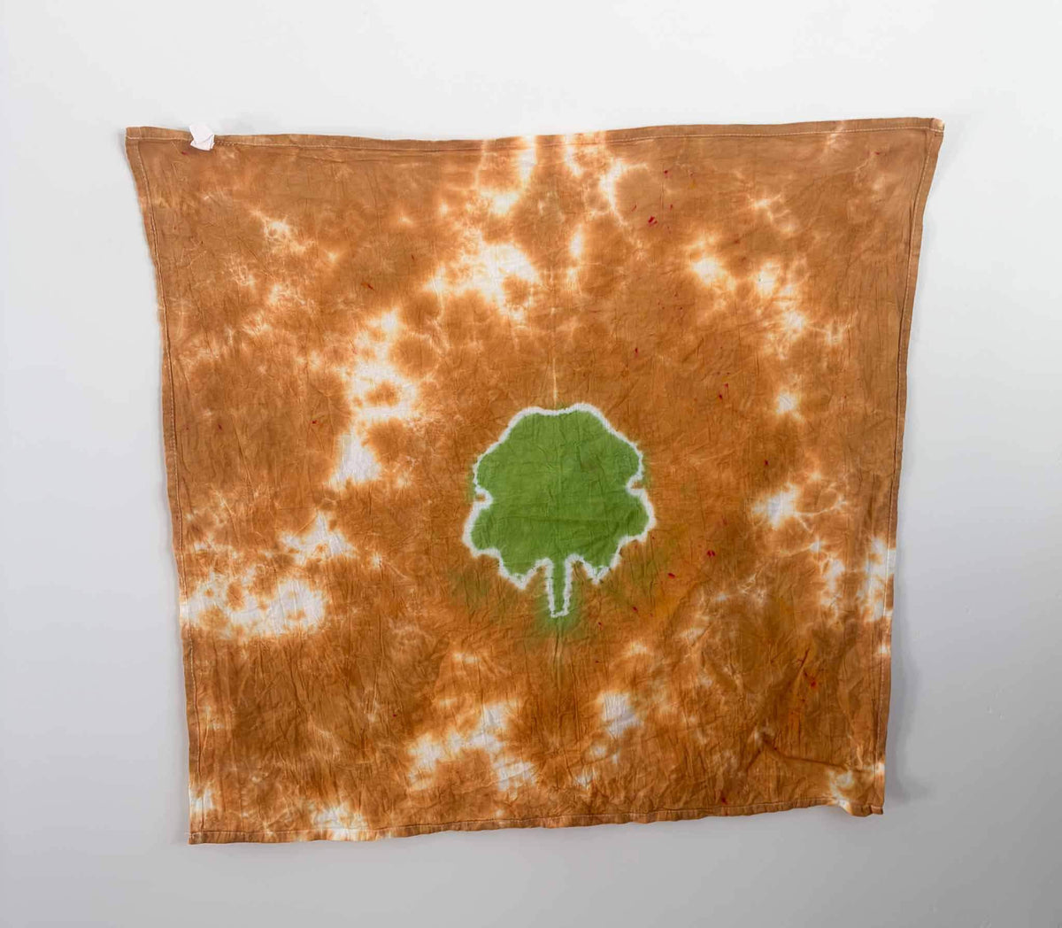 Green clover tie dye tea towel hanging flat, rust brown background, 27x27 cotton