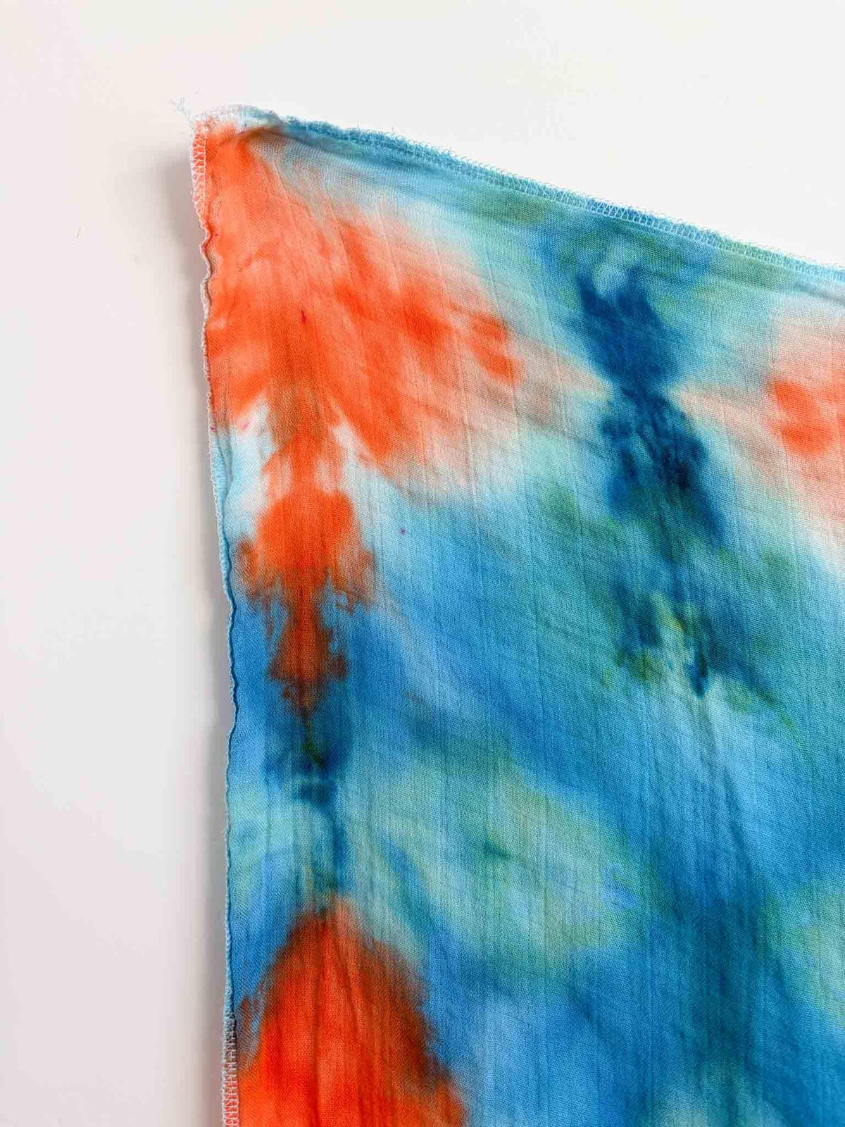 Close up of serged edge on hand dyed bamboo gauze swaddle showing orange and blue diamond pattern