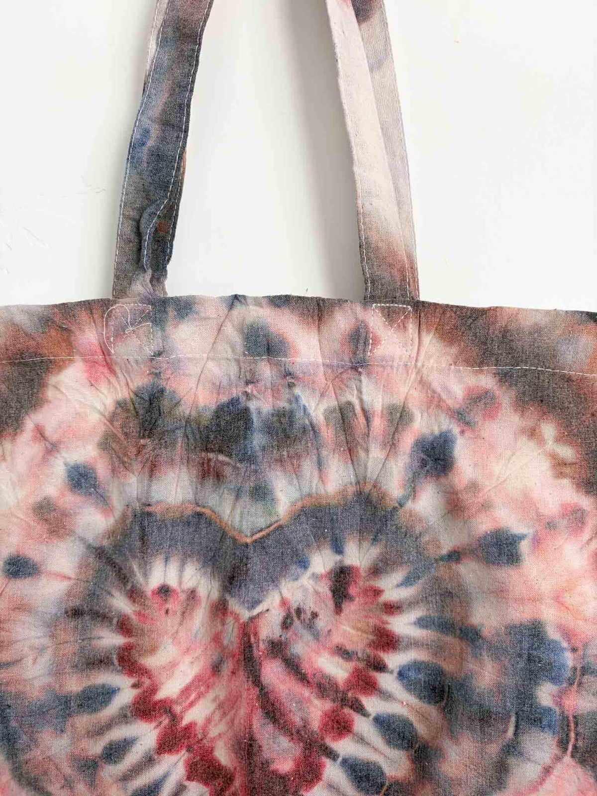 Close up of tote bag handles and top of heart fold ice dye pattern in navy and burgundy