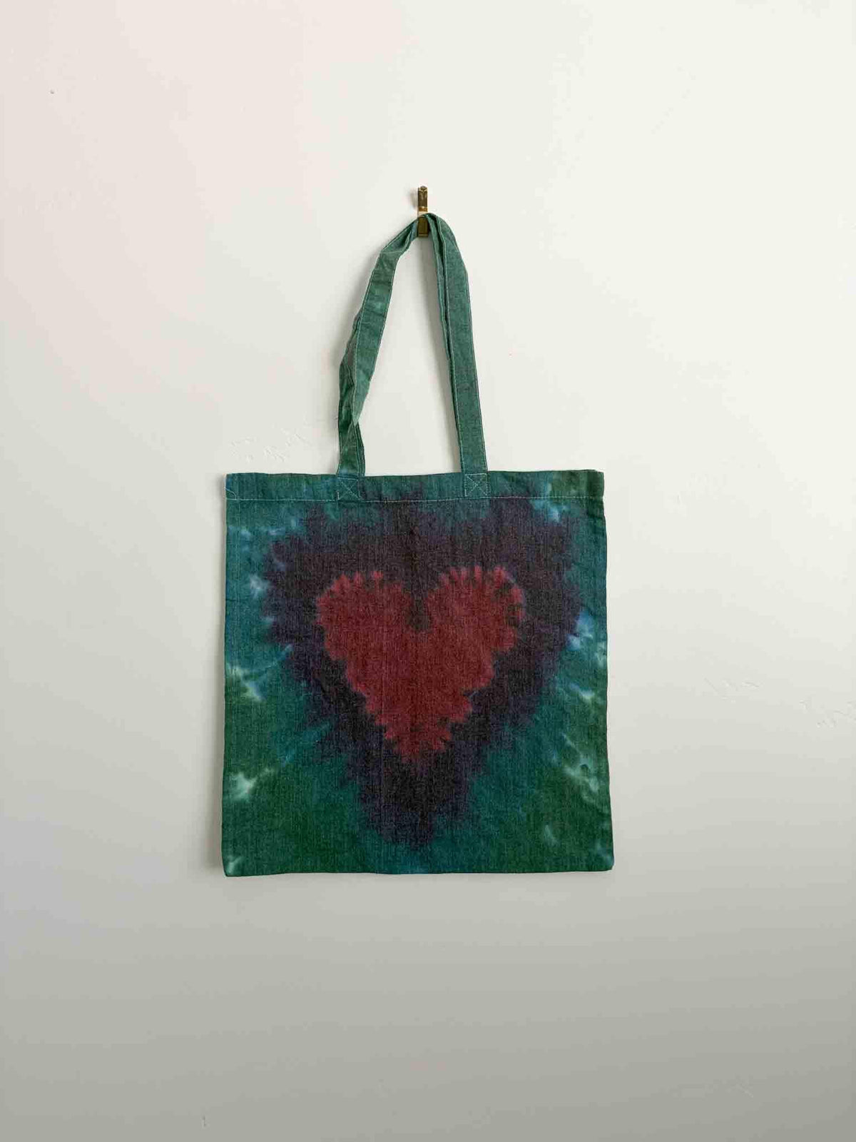 Crimson heart tie dye tote bag on green and purple background, cotton canvas with long handles