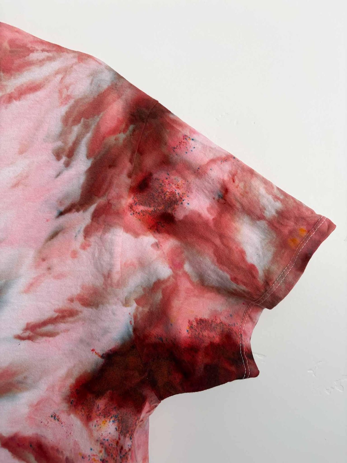 Sleeve detail of rust pink ice dye tie dye v-neck shirt showing color speckles