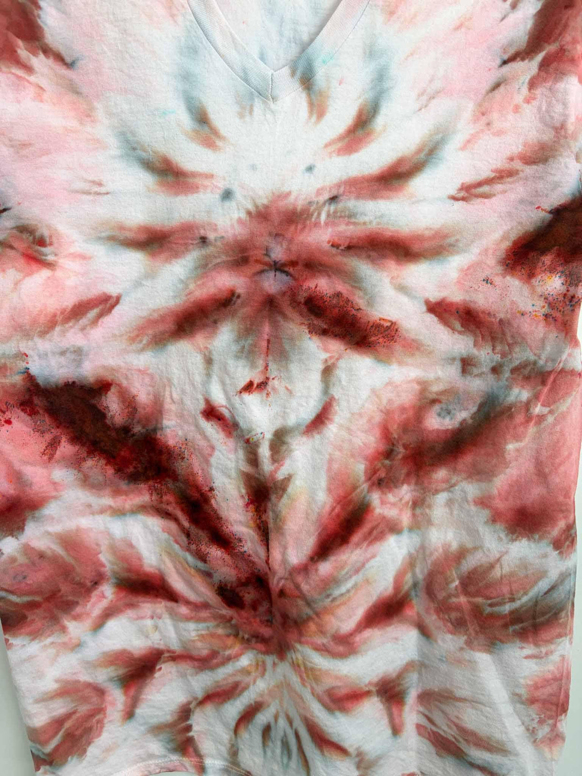 Close up of rust and pink ice dye starburst pattern on tie dye v-neck shirt