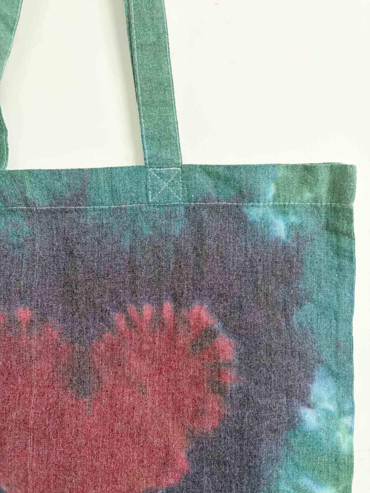 Close up of tote bag handle attachment and top of heart tie dye pattern in green and crimson