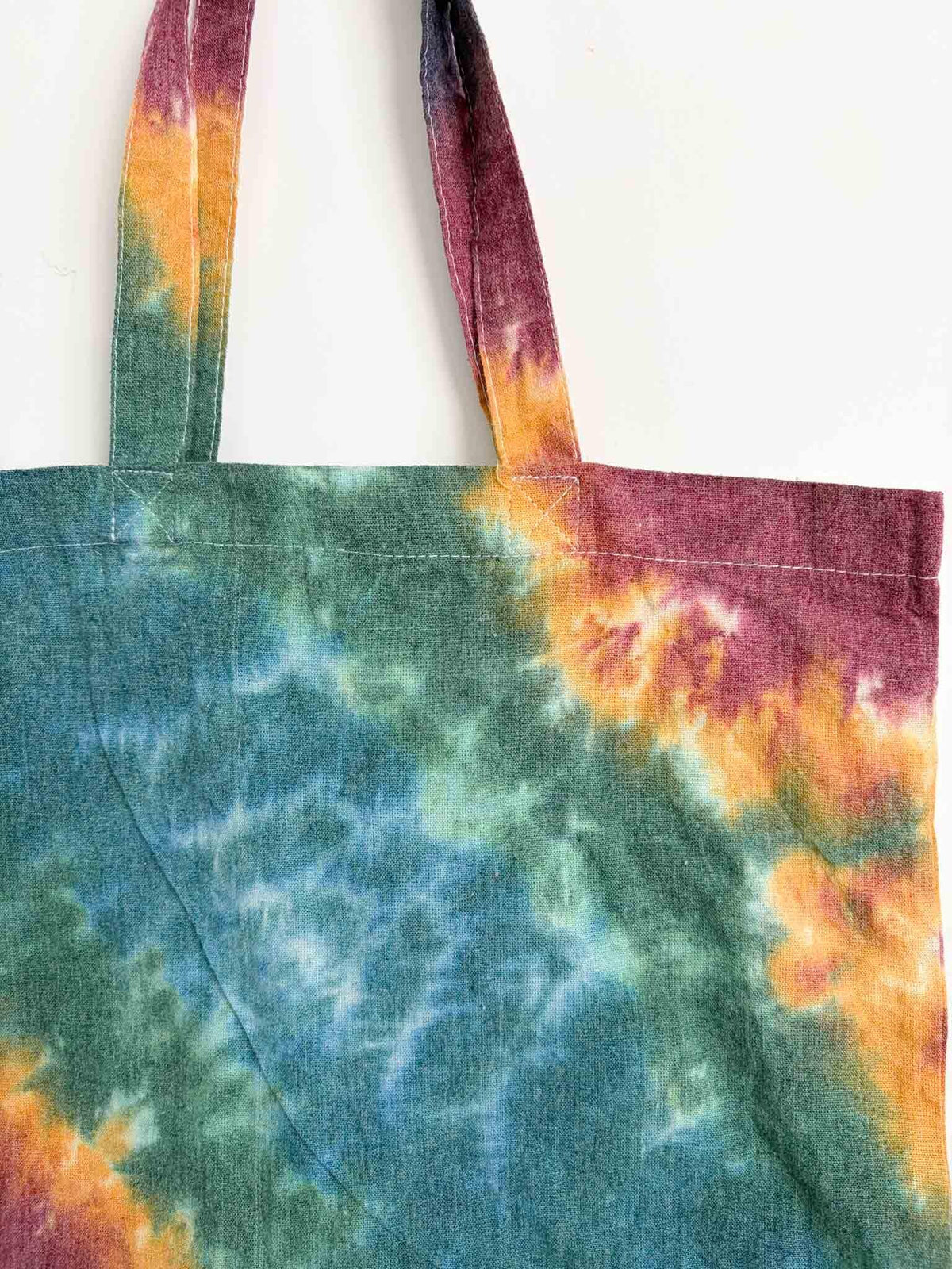 Close up of tote bag handles and top corner showing magenta, gold, and teal tie dye pattern