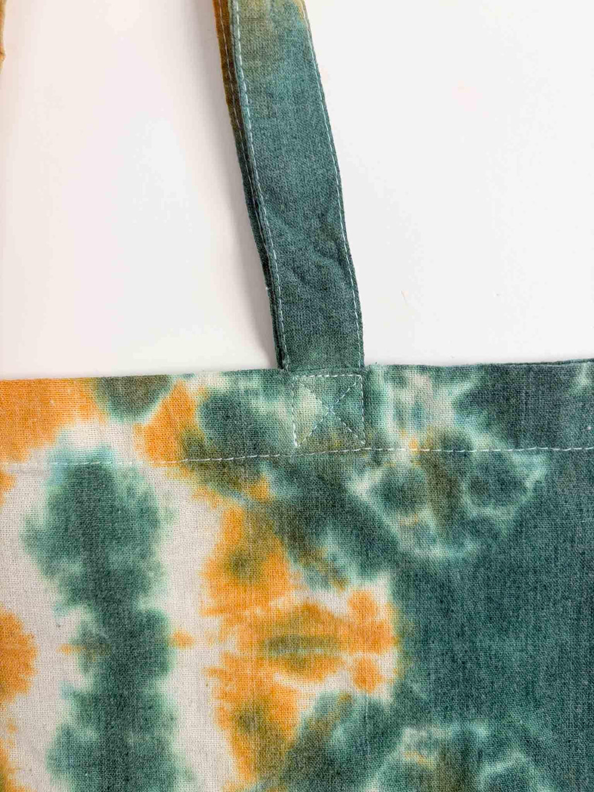 Close up of tote bag handle attachment and shibori pattern in forest green and mustard gold
