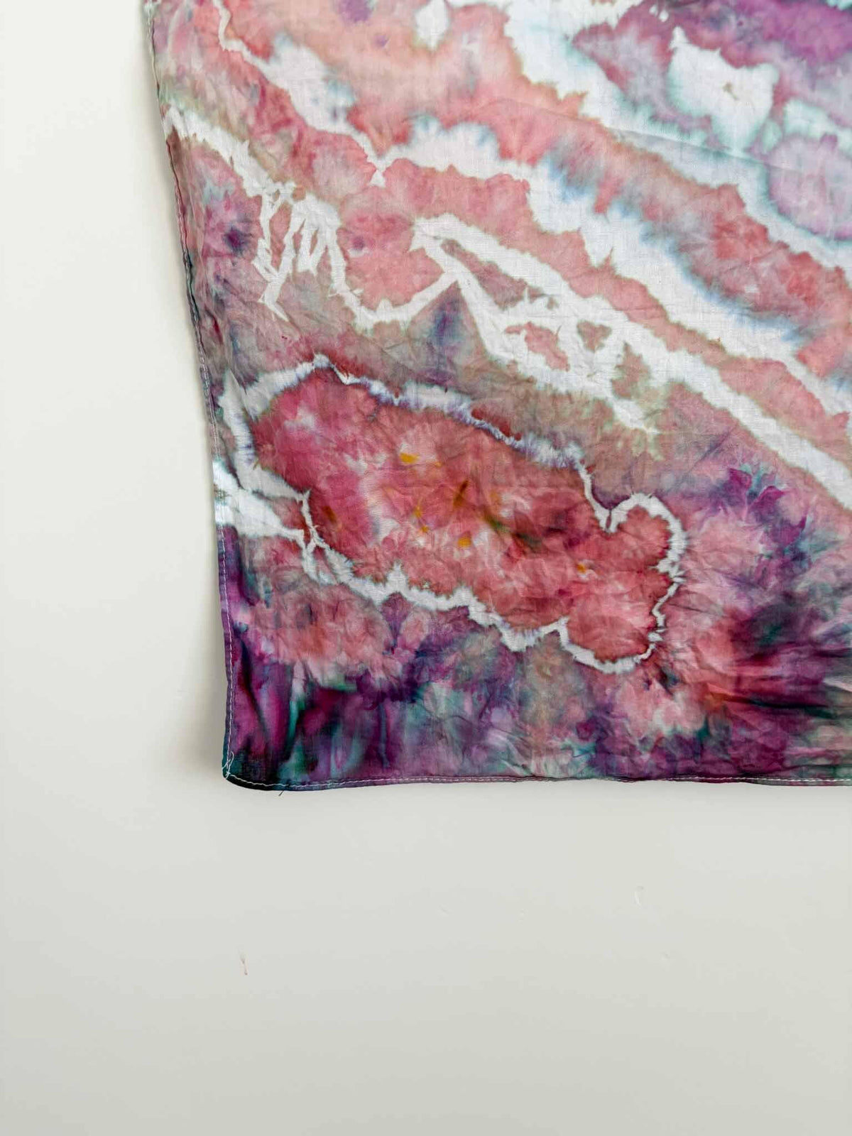 Close up corner detail of ice dyed bandana showing coral pink and mauve tie dye pattern with white crackle lines