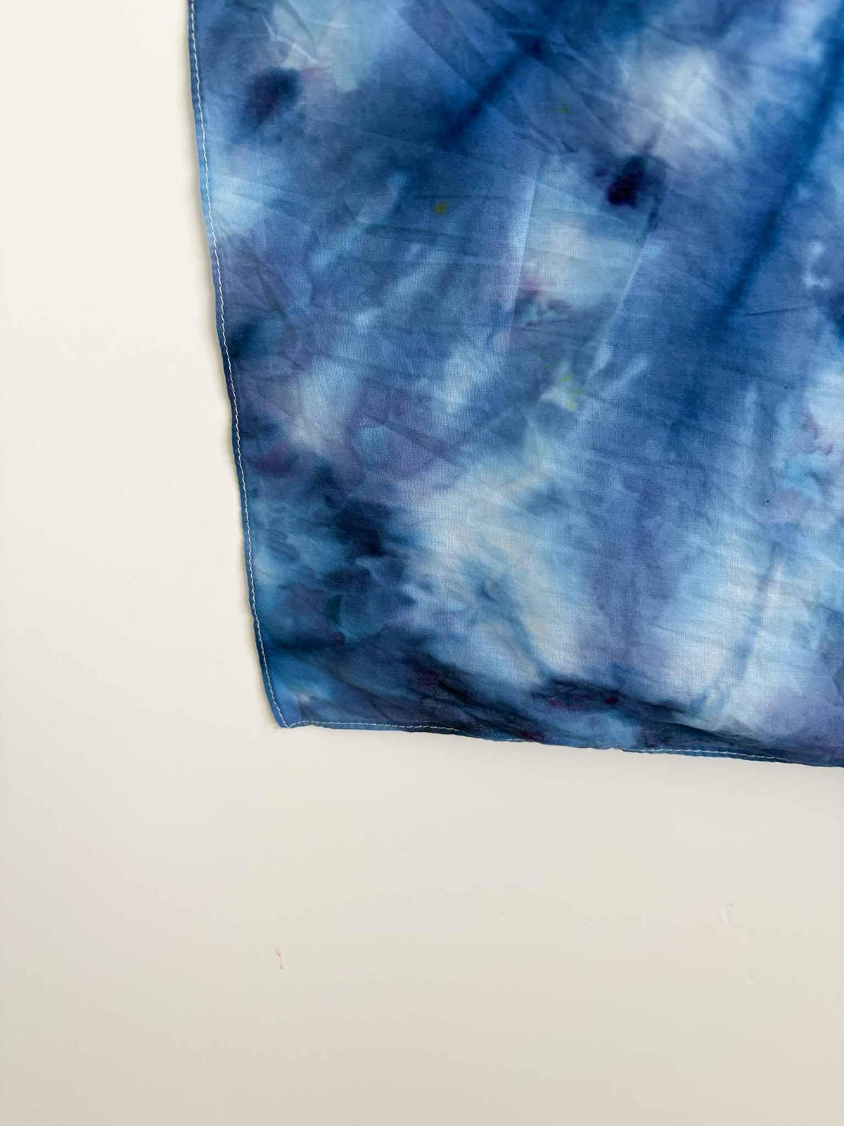Close up corner detail of hand dyed bandana showing denim blue tie dye pattern with white hemmed edge