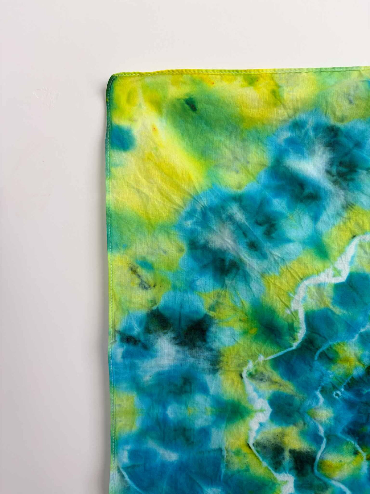 Corner detail of green blue tie dye bandana showing yellow and teal ice dye colors
