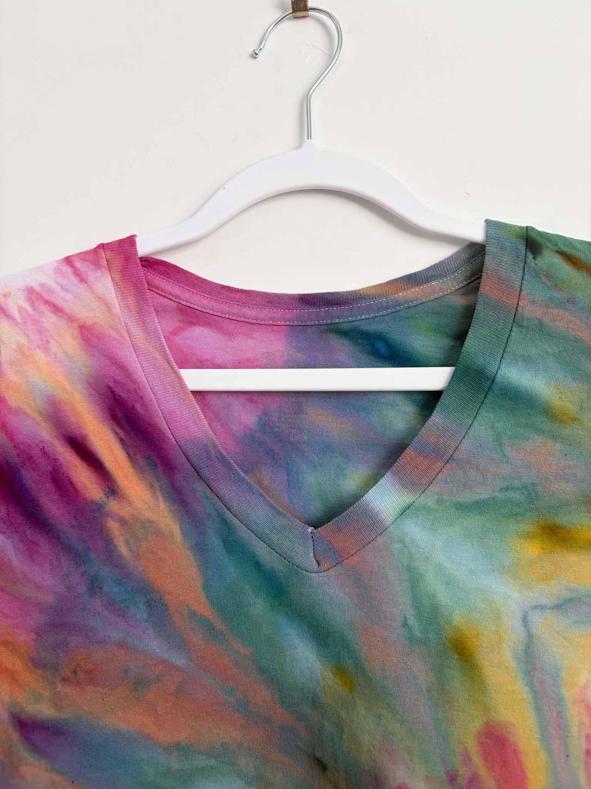 Close up of pink teal and yellow ice dye fern fold pattern on v-neck shirt