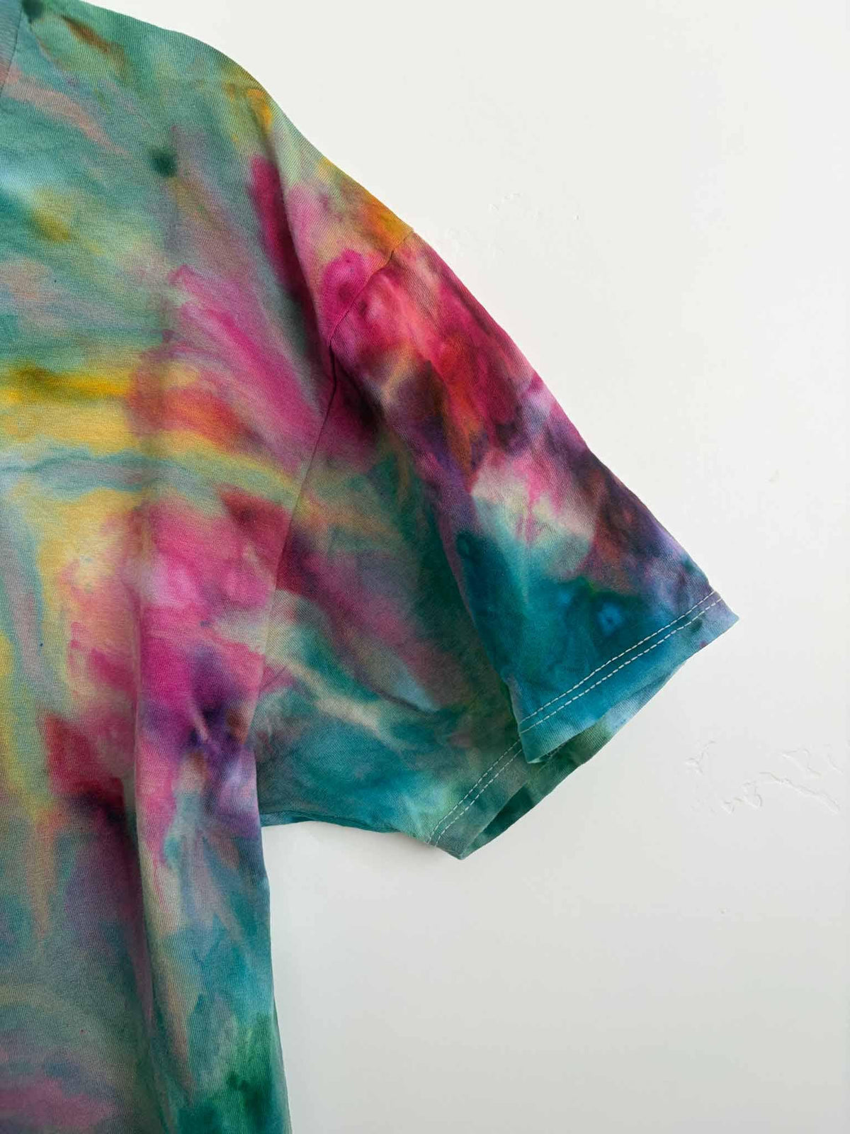 Sleeve detail of rainbow ice dye fern fold tie dye shirt showing pink and teal
