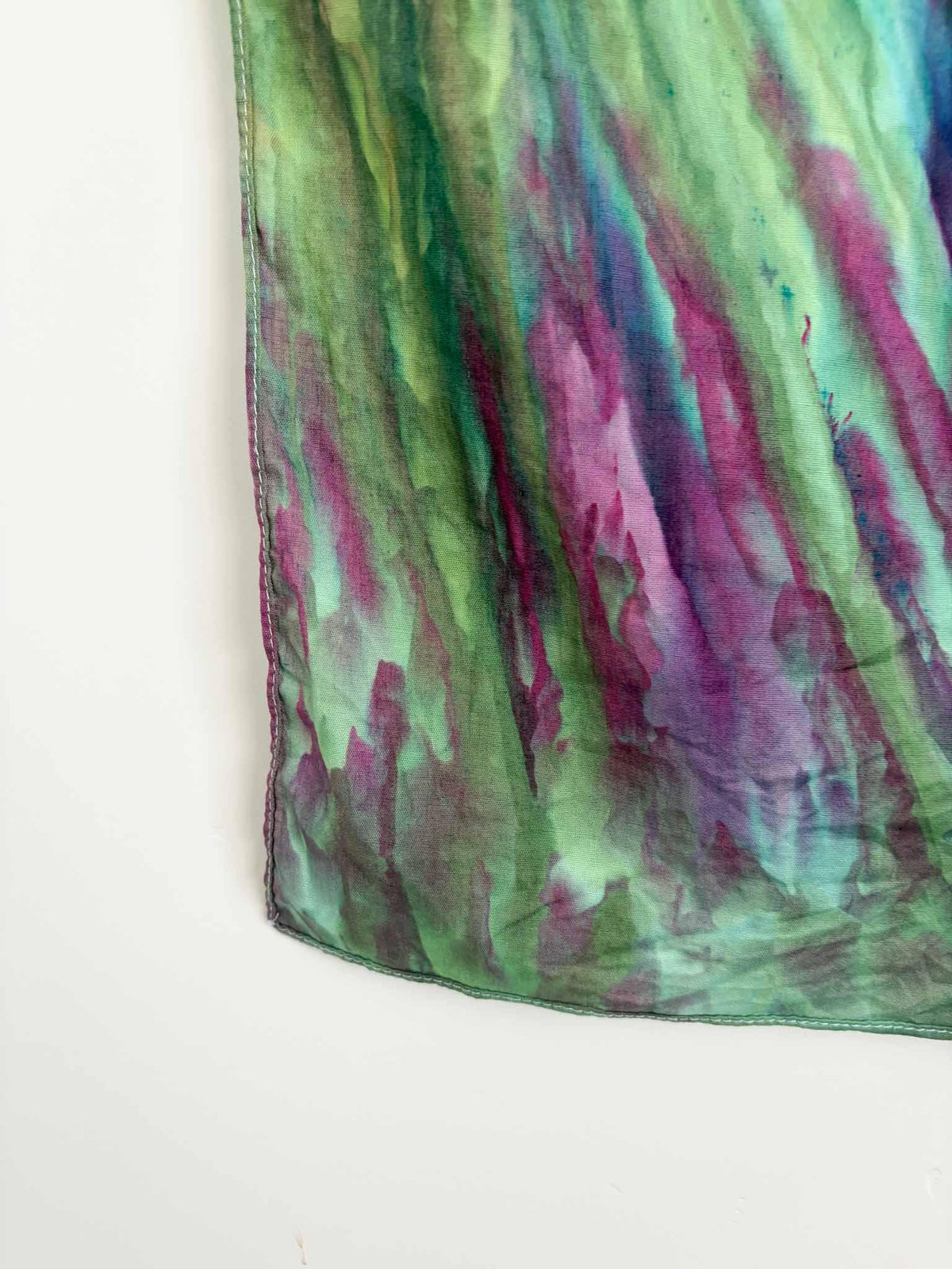 Close up corner detail of hand dyed bandana showing green and magenta diagonal stripe pattern with white hemmed edge