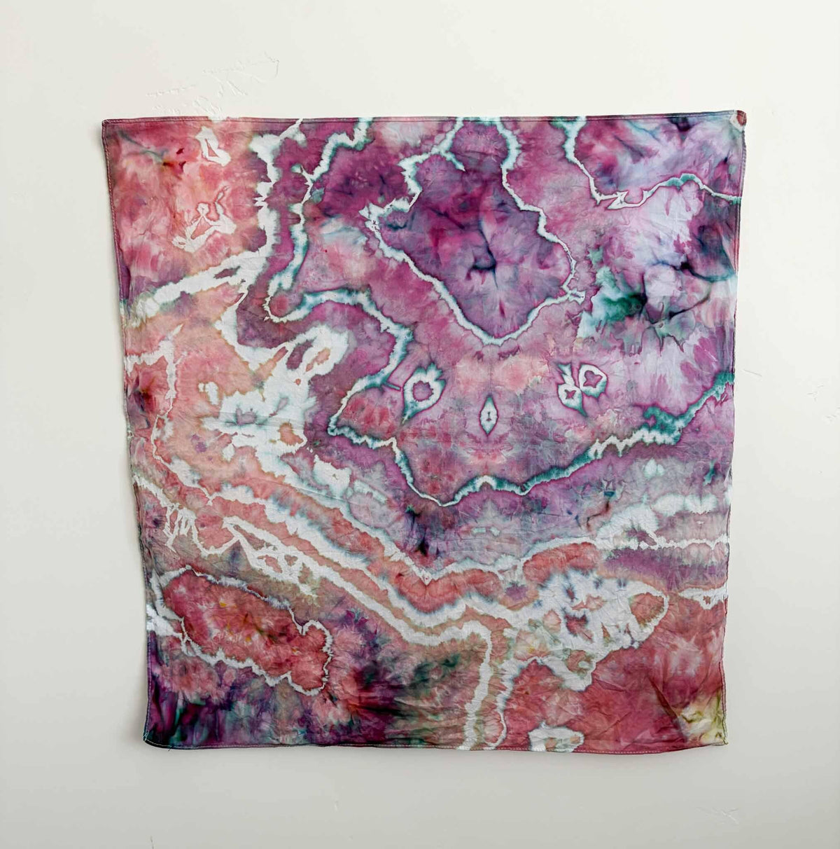 22x22 inch ice dyed cotton bandana in pink and magenta geode pattern with teal crackle veining hanging on a wall