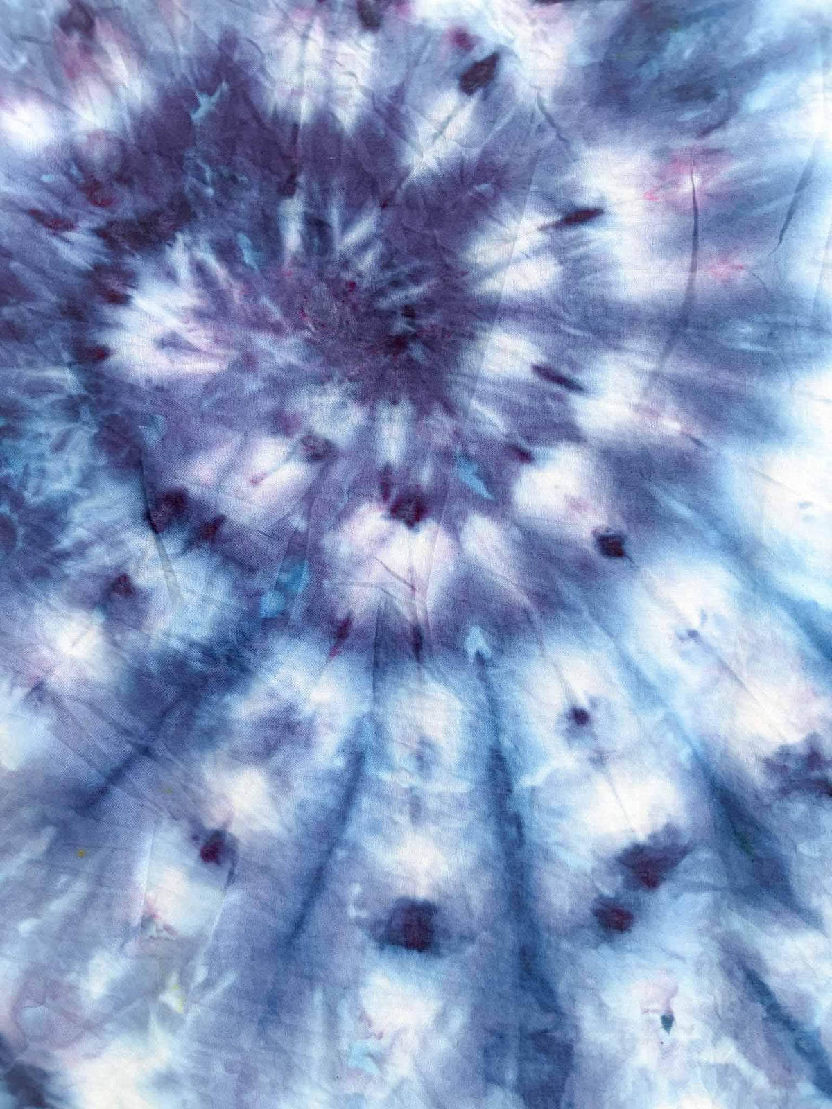 Close up center detail of ice dyed cotton bandana showing dark indigo starburst spiral pattern with blue rays
