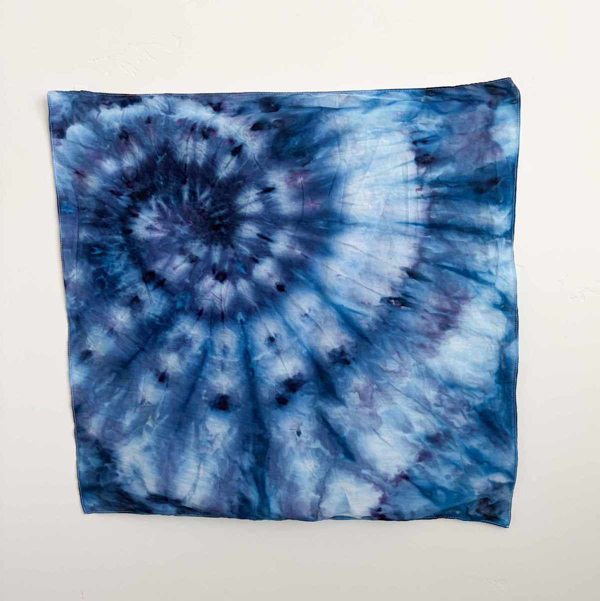 22x22 inch ice dyed cotton bandana in blue and indigo spiral swirl pattern hanging on a wall