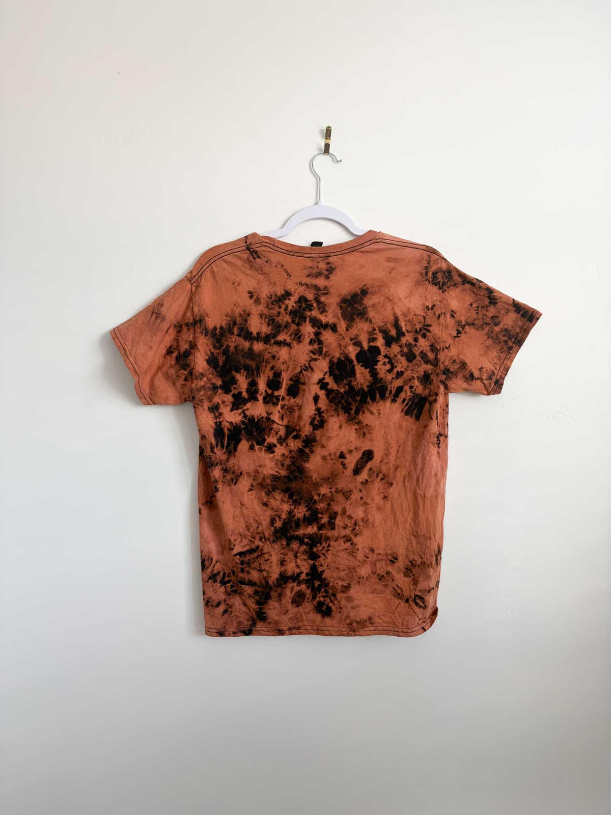 Back view of rust orange and black bleach crumple tie dye t-shirt hanging on white hanger